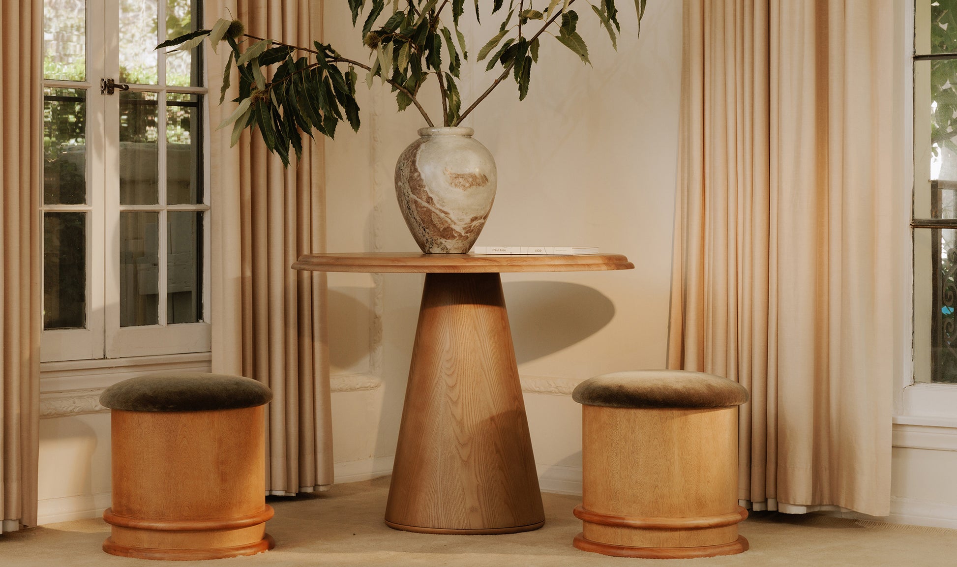 Wooden table with a vase and two stools in a room with curtains