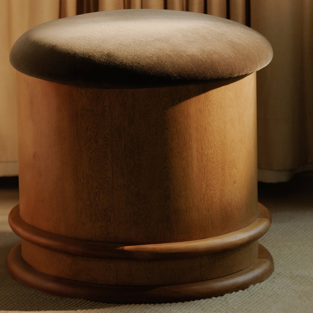 Wooden stool with a round top and base in a room with beige curtains.