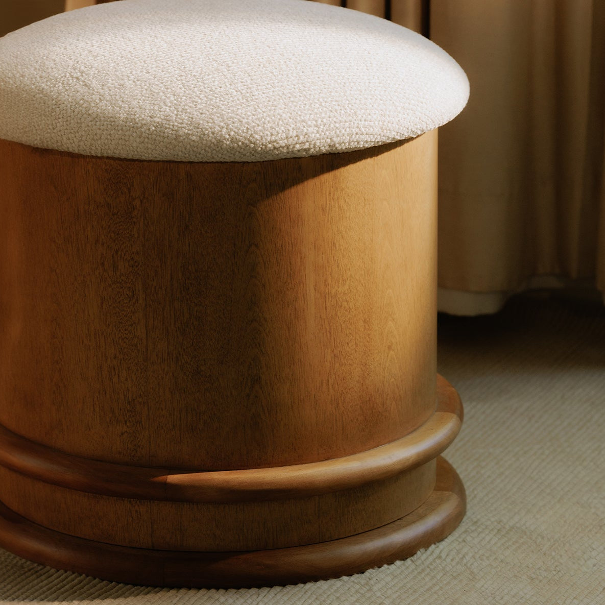 Wooden ottoman with a textured white cushion on a carpeted floor.