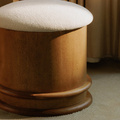 Wooden ottoman with a textured white cushion on a carpeted floor.